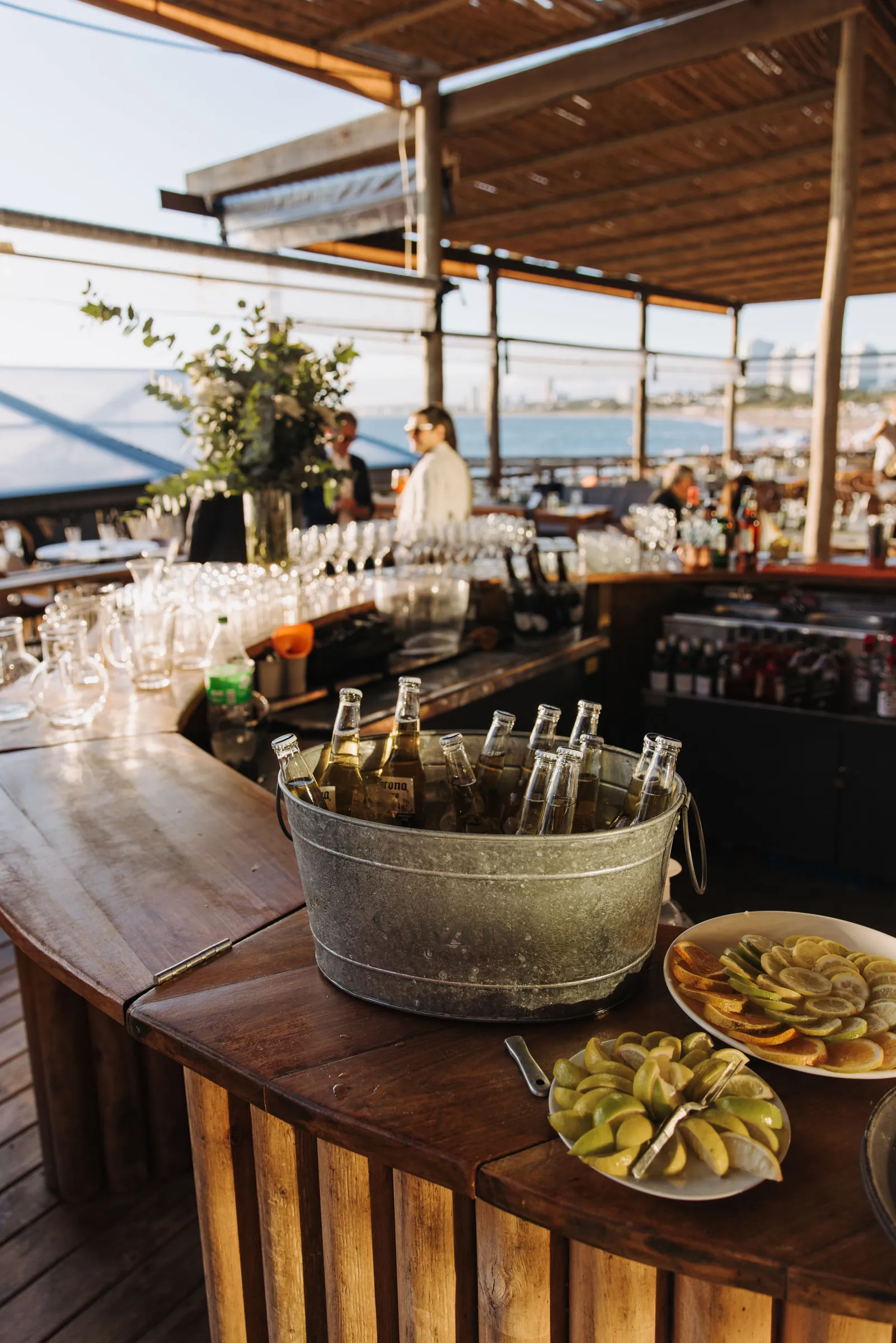 Balde con botellas sobre la barra de madera de la terraza, con frutas cortadas al costado