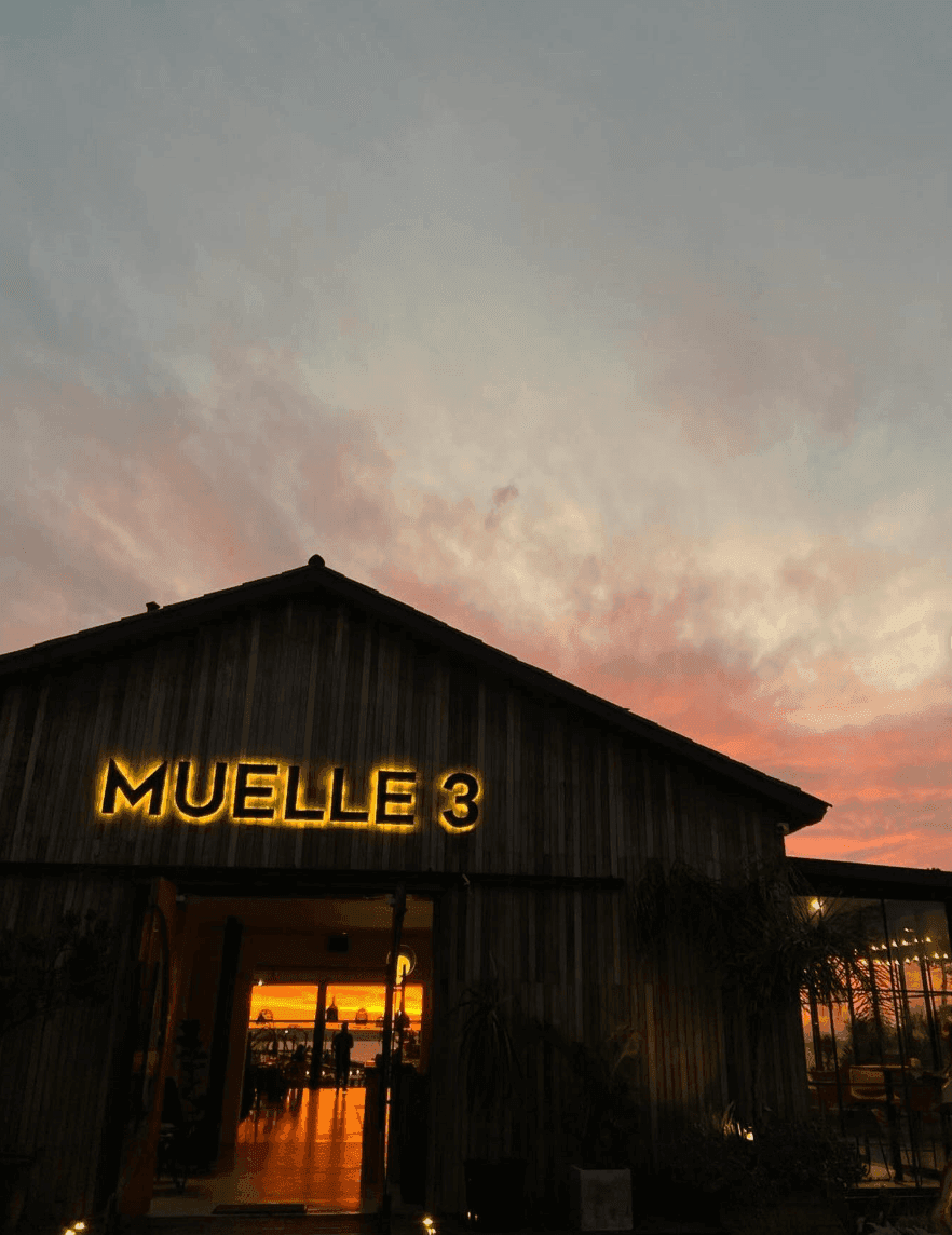 Fachada de Muelle 3 al atardecer, cartel retroiluminado contra el cielo