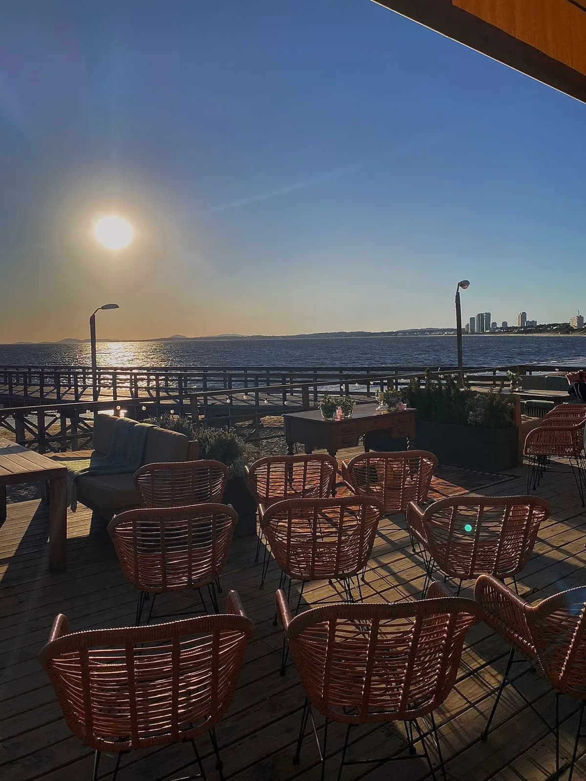 Sillas de mimbre en la terraza de Muelle 3, con el mar y el atardecer de fondo