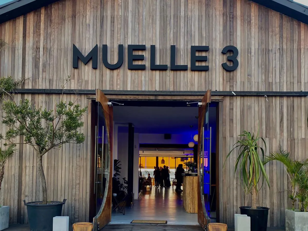 Fachada de madera de Muelle 3 con el cartel y la puerta abierta, de día